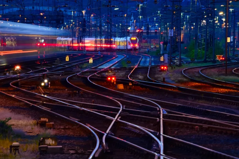 Railway junction at dusk with curving tracks, signal lights, and a blurred passing train